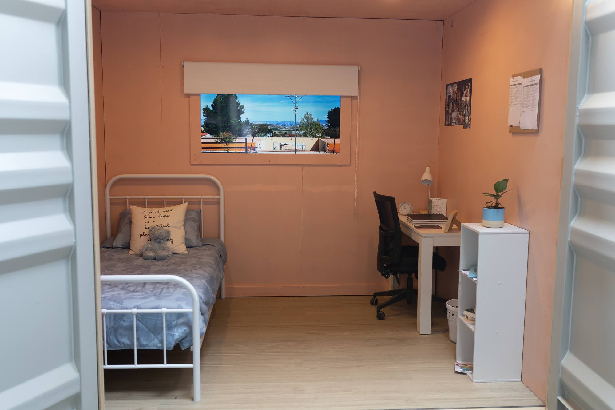 Inside the container: the warm bedroom with a bed, desk, and window, the room that could keep a child at home