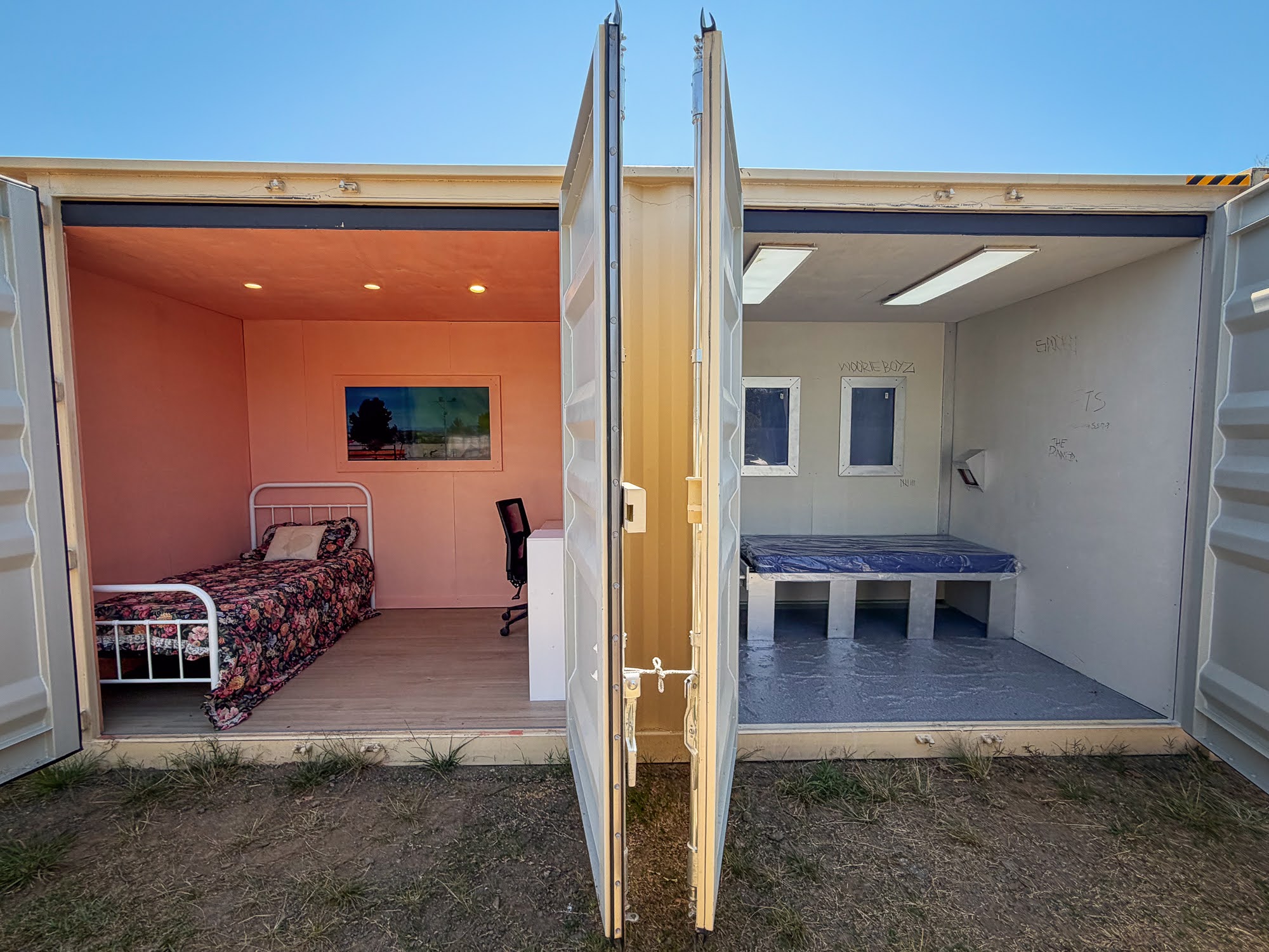 Inside the container: a bare detention cell with a concrete bed, next to a warm bedroom